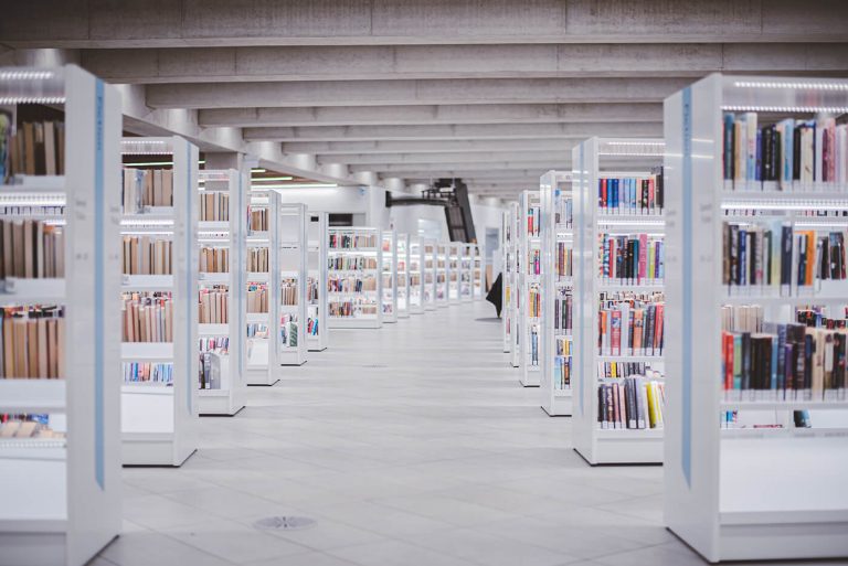 A look down a hallway between rows of white shelves full of books in a Calgary Public Library.