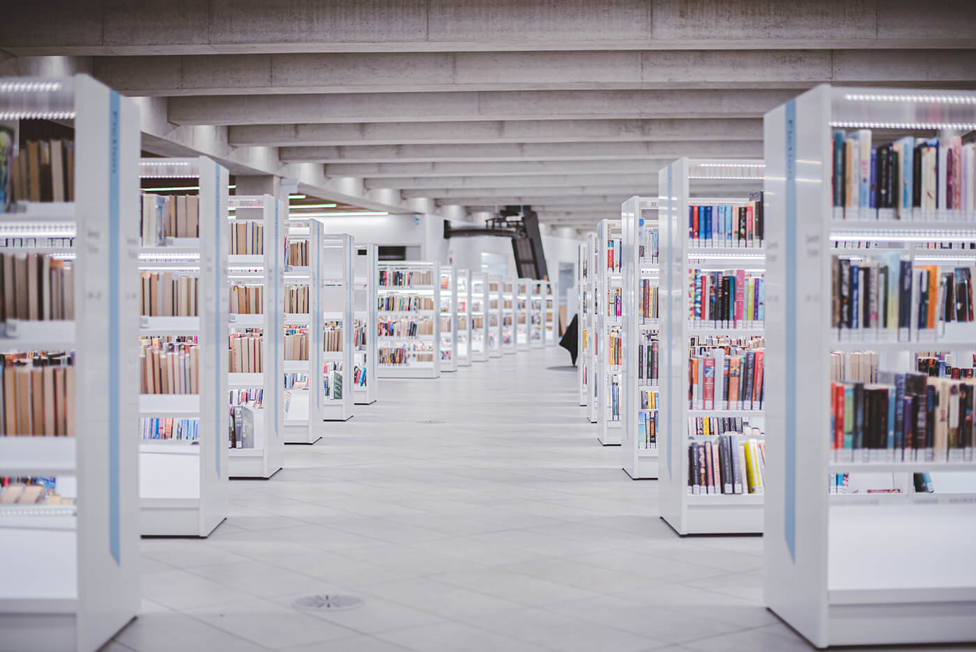 A look down a hallway between rows of white shelves full of books in a Calgary Public Library.